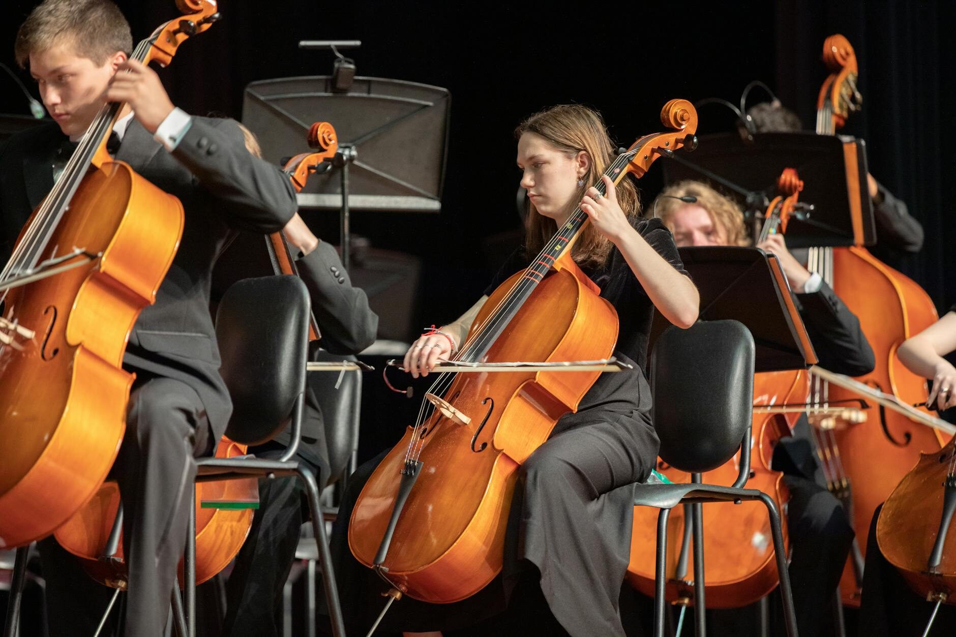 Cello section performing in concert dress under warm amber stage lighting