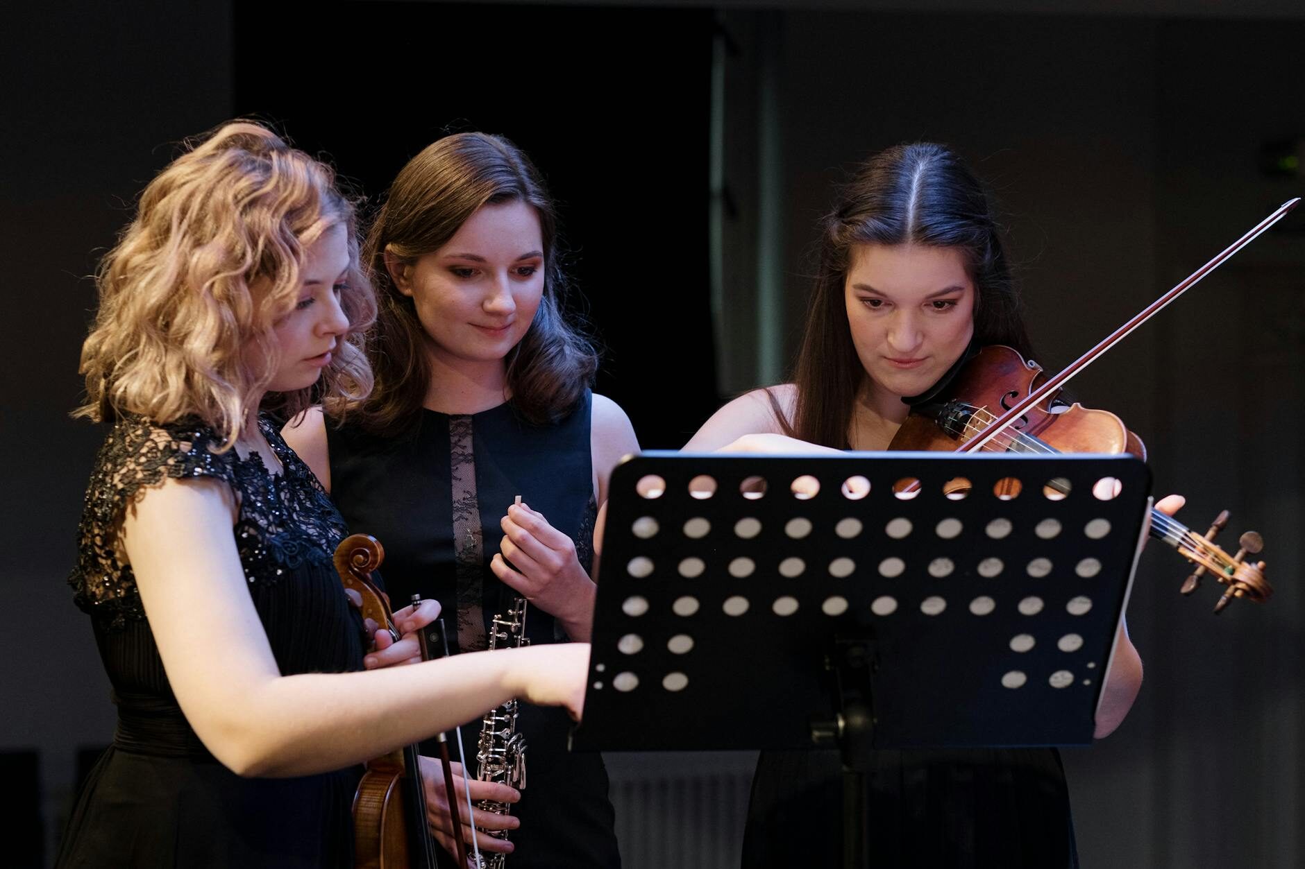 Three musicians studying sheet music together in a rehearsal setting