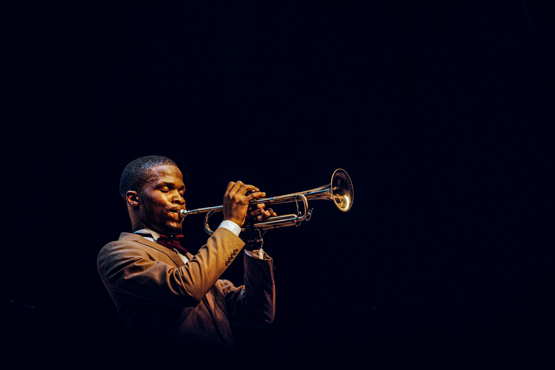 Trumpeter performing on a dramatic dark stage with warm side lighting