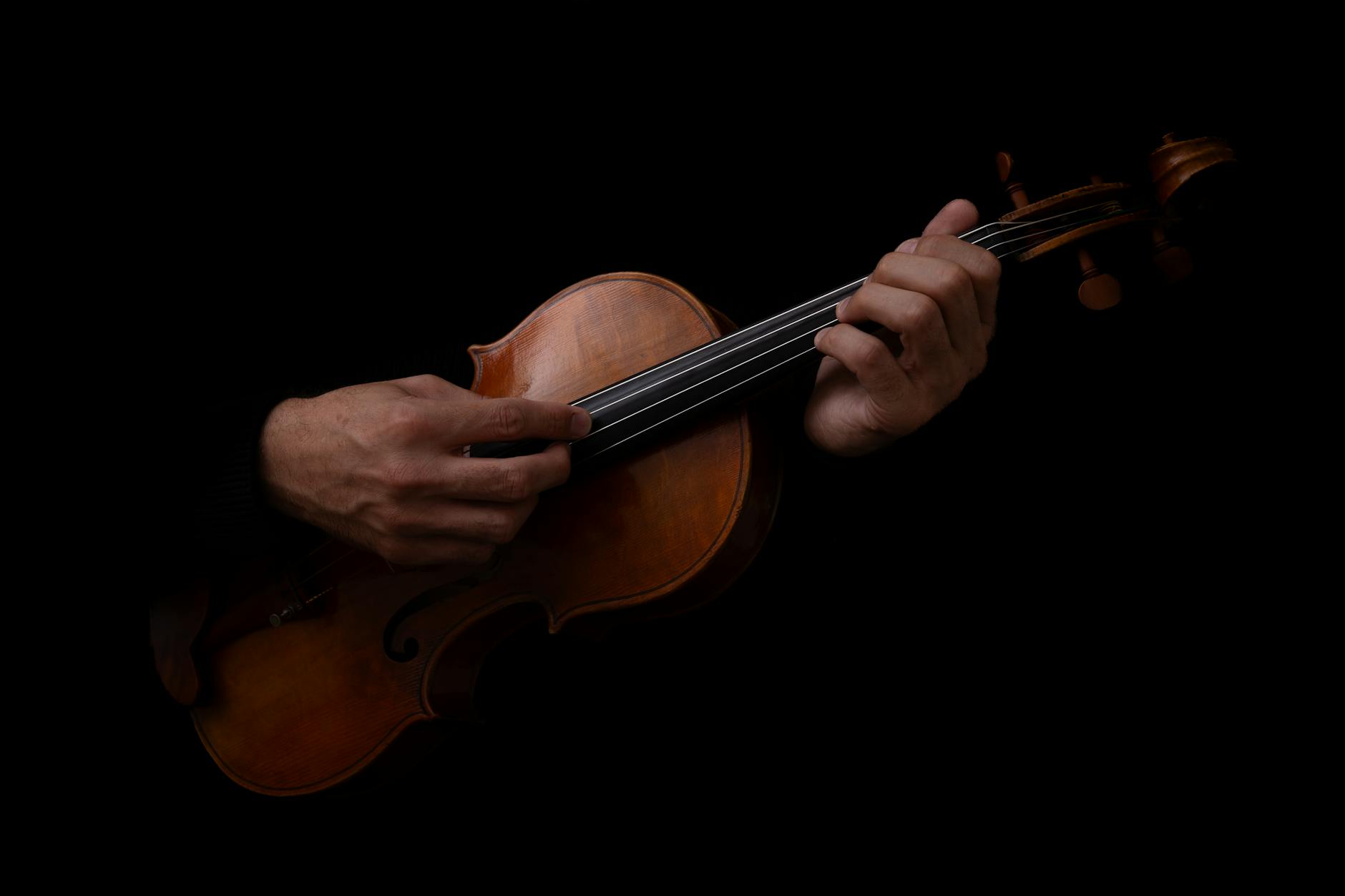 Violin held in warm amber light against a black background