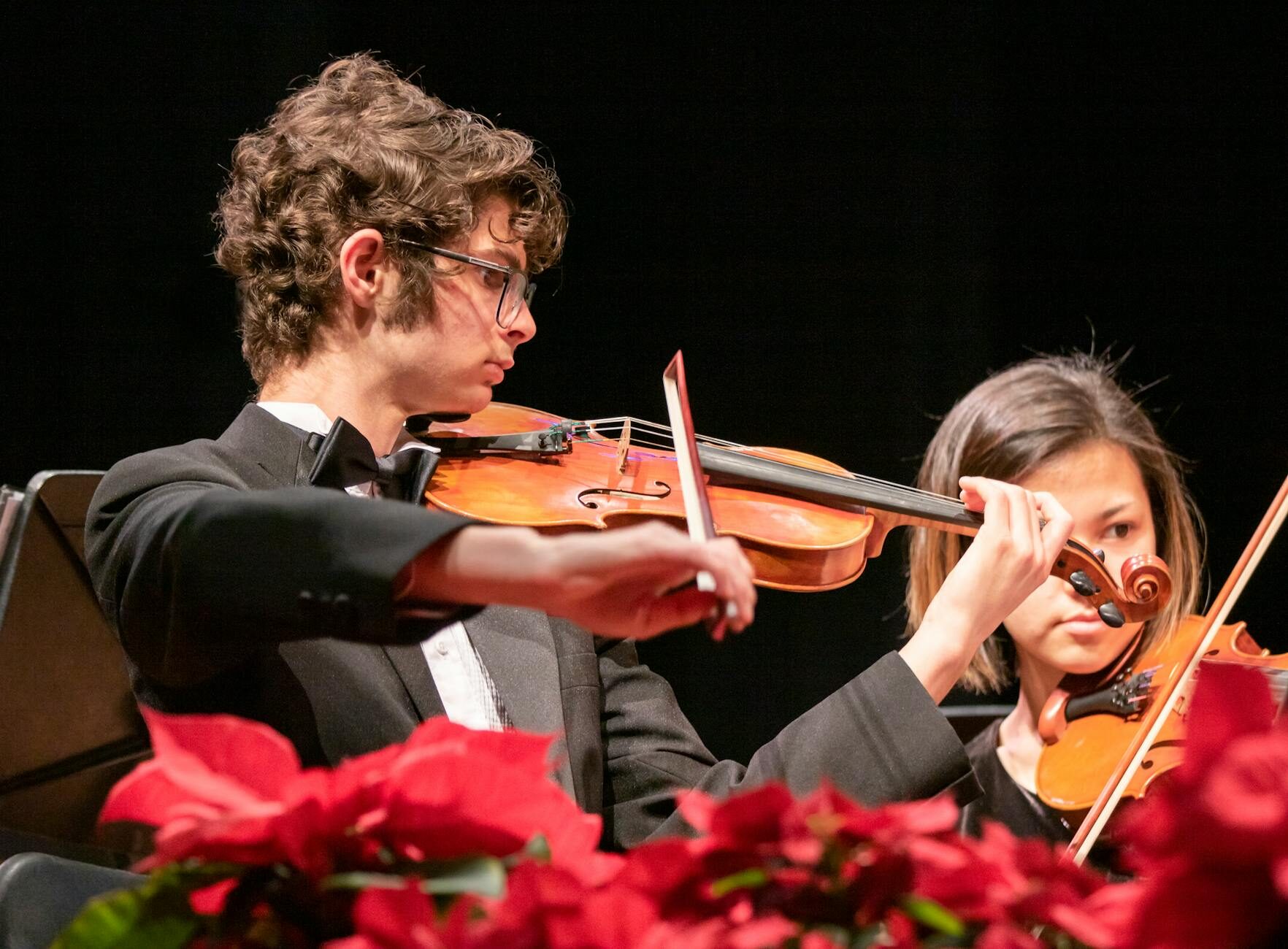 Violinists performing at a Christmas concert with red poinsettia flowers